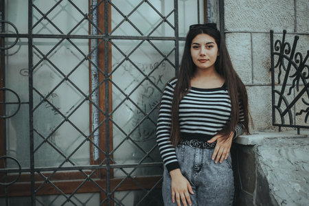 Casual woman posing near a stone wall, representing independence and urban life.の写真素材