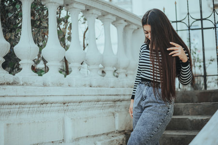 Woman standing by a fence, lost in deep thought in an urban setting.の写真素材