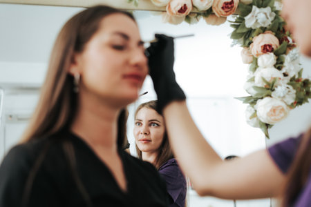 Eyebrow correction is captured with the cosmetologist's face reflected in the mirror, highlighting...