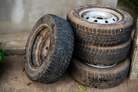 Three used tires stacked outdoors, showing signs of wear and dust, suitable for automotive...