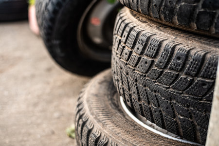 A stack of worn tires in a garage setting, showing visible wear and dirt, ideal for automotive and industrial concepts.の写真素材