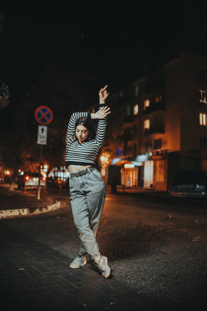A stylish brunette poses in the middle of an empty city street at night, with glowing autumn streetlights adding charm and urban atmosphere.の写真素材