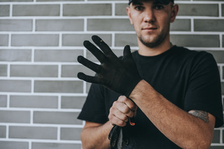 A man is putting on protective gloves, symbolizing safety and preparation for physical work.