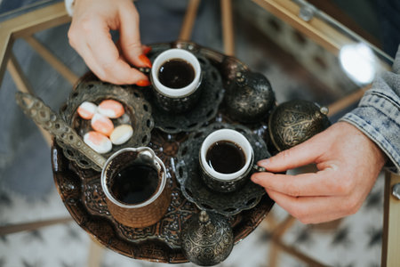 A person is holding two cups of coffee and a tray with a variety of candiesの写真素材