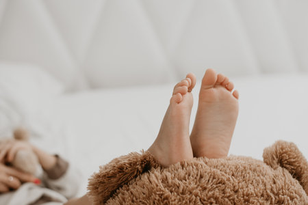 Little boy lying on bed with bear, feet in focus, cozy atmosphereの写真素材