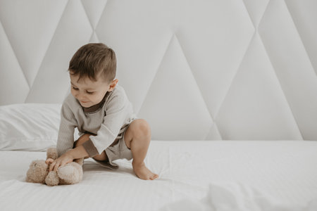 A young boy is engaged in playful exploration with a soft toy on a big, white bed, looking curious and full of energy.の写真素材