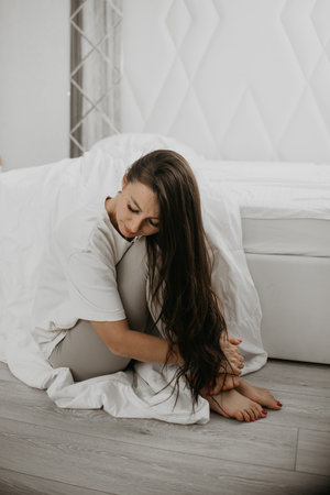 Woman stretching her legs while sitting in bed, capturing a calm and cozy morning atmosphere in a serene bedroom.の写真素材