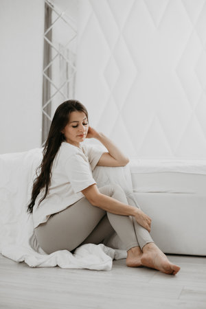 Woman sitting in bed and gently touching her hair, enjoying a relaxed morning moment in a cozy, minimalist space.の写真素材
