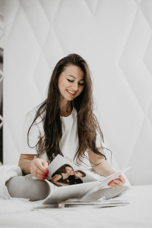 Smiling woman sitting on bed, reading a book, capturing a calm and relaxed morning vibe in a minimalist bedroom.の写真素材