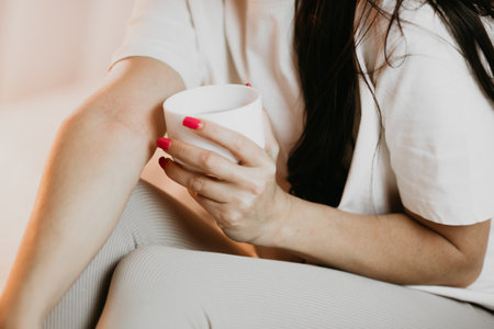Close-up of a woman sitting with her legs crossed, holding a warm cup of coffee in a relaxed, cozy atmosphere.の写真素材