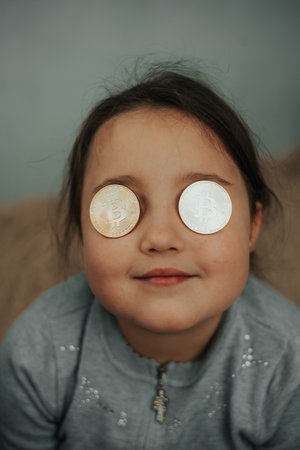 Young girl playing with cryptocurrency coins, holding them in front of her eyes like glasses.の写真素材