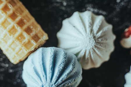 A composition of crisp wafers and pastel-colored meringues on a black surface with sugar dusting.の写真素材
