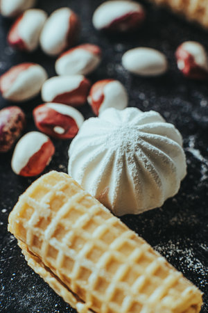 A composition of crisp wafers and pastel-colored meringues on a black surface with sugar dusting.の写真素材