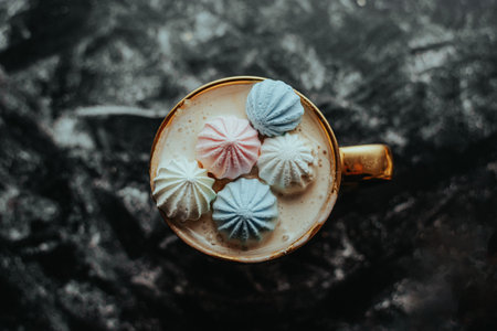 A top-down view of a golden cup filled with coffee and topped with colorful meringues on a dark, textured surface. The blend compositions elegance and rustic charm.の写真素材
