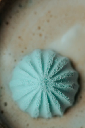 A delicate blue meringue sits atop frothy coffee, slightly melting into the creamy texture. The close-up shot captures the contrast between the airy dessert and the rich beverage.の写真素材