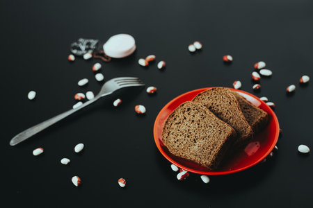 A plate with brown bread slices and scattered candies on a black table.の写真素材