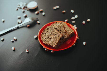 A plate with brown bread slices and scattered candies on a black table.の写真素材