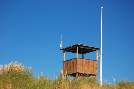 Wooden stand and flagpost against blue sky behind duneの写真素材