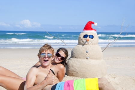 Pretty couple having fun at beach with perfectly build snowman made out of sand wearing sunglassesの写真素材