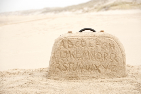 Suitcase with alphabet letters writing made out of sand on beachの写真素材