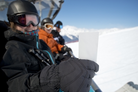 Girl holding ski pass while sitting with friends in chair lift smiling. Concept to illustrate ski admission feeの写真素材