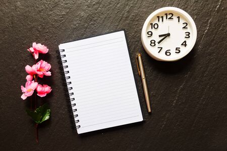Flat lay of blank note pad, pen, clock and cherry blossom flower.の写真素材