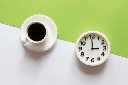 Flat lay of round white alarm clock and cup of coffee on split color green and white background.の写真素材