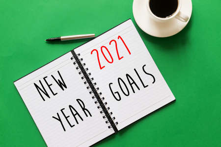 Flat lay of Notebook with words written - New year, 2021 Goals. Coffee and pen on green background....