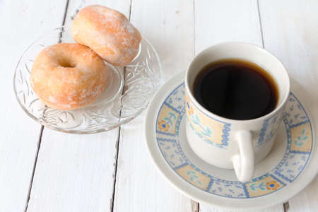 Donut coated with sugar served with coffee on white wooden tableの写真素材