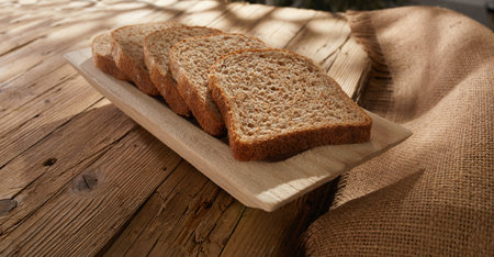 sliced bread on a wooden tray. breadboard on an old wooden table with cracks and rough fabric. baking in sun spots. rural lifestyle.の写真素材