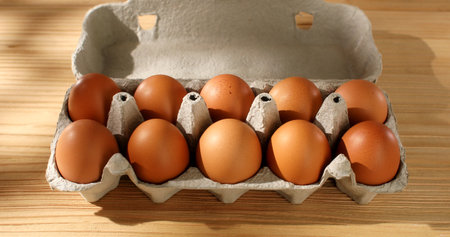 Package of Eggs. Chicken Eggs in a cardboard box on a wooden background. Close up. High angle view....
