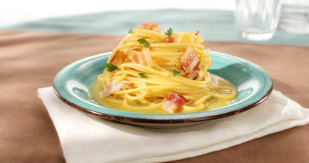 Spaghetti carbonara. Pasta with pancetta, egg, parmesan cheese. Green plate on brown background. Hard light, angle view. Traditional italian cuisine. Pasta alla carbonara.の写真素材