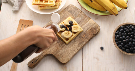 Belgian waffle with banana slices topped with chocolate topping. Breakfast preparation. Sweet food.の写真素材