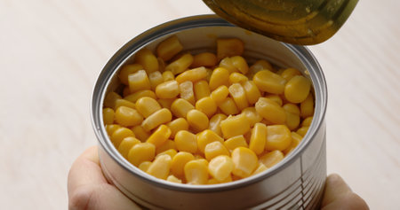 Womens hands open a can of corn. Food preparation with canned vegetables.の写真素材