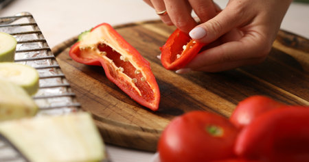 Slicing vegetables. Female hands cut sweet Red Bell Pepper on a cutting board. Cooking in the...