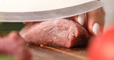 Cutting raw meat. Female hands cut fresh beef on a wooden chopping board. Cooking in the kitchen. Food preparation.の写真素材