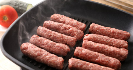 Raw minced meat sausages are fryed on a grill pan with steam or smoke. Frying traditional Balkan chevapi. Cooking food.の写真素材