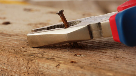 Close-up of Pliers Pulling a Rusty Nail out of an old Wooden Board.