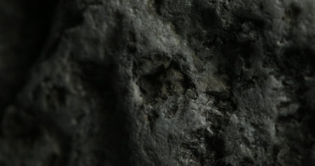 A detailed close-up of a dark gray stone, showcasing its rugged, uneven surface with deep crevices and weathered textures. The stones roughness hints at long exposure to natural elements.の写真素材