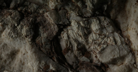 Detailed view of a rugged surface of rock, highlighting its uneven texture, natural coloration, and small cracks. The raw beauty of natures formations with a focus on the surfaces intricate details.の写真素材