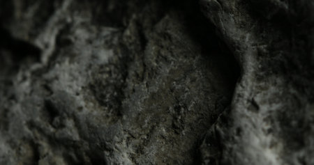 A detailed close-up of a dark gray stone, showcasing its rugged, uneven surface with deep crevices and weathered textures. The stones roughness hints at long exposure to natural elements.の写真素材