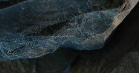 Close-up of dark slate rock with jagged edge and soft bluish shadowsの写真素材