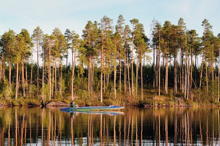 The fisherman floats on a canoe along coast of evening lakeの写真素材