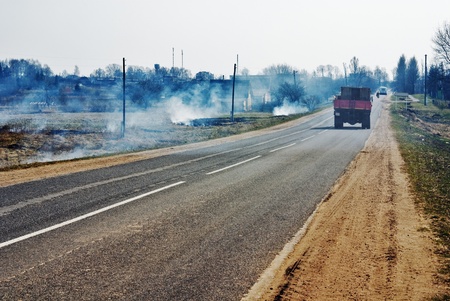 The spring asphalt road near which burns a dry grassの写真素材