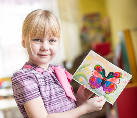 portrait of a cheerful smiling girl holding a bright colorful picture of butterfly painted colors, plasticine and crayons in kindergarten - Moscow, Russia - February 4, 2016のeditorial素材