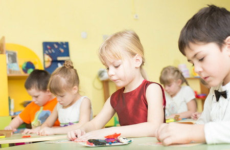 a portrait of a happy smiling girl draws bright colorful picture and sculpts from clay in kindergarten - Russia, Moscow - February 04, 2016のeditorial素材