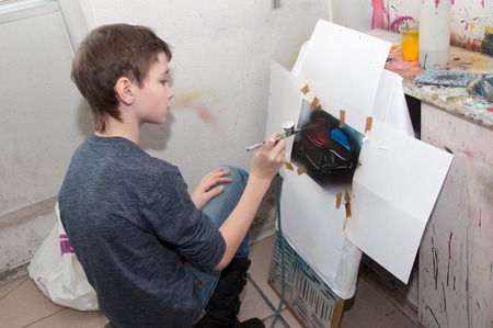 a boy teenager engaged in airbrushing paint brightly colored pictures in a artistical studio - Russia, Moscow - January 24, 2016のeditorial素材