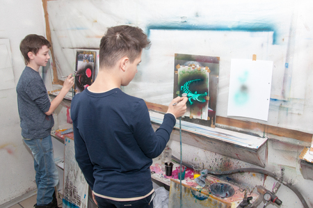 a group of children of teenagers engaged in airbrushing paint brightly colored pictures in a artistical studio - Russia, Moscow - January 24, 2016のeditorial素材
