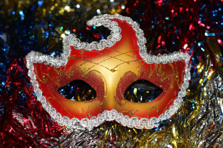 a bright red - gold mask on the background of multi-colored Christmas-tree tinselの写真素材