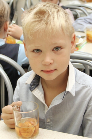 merry schoolboy Sitting At Table In School Cafeteria Eating Meal. drinking juice - Russia, Moscow, the first High School, the first class b - September 30 2017のeditorial素材